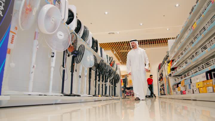 استكشاف الخيارات المتاحة قبل الشراء، رجل عربي خليجي اماراتي يرتدي الزي التقليدي يتجول داخل متجر أجهزة منزلية حديث، قسم المراوح الكهربائية