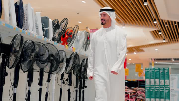 تقييم المنتجات قبل الشراء، رجل عربي خليجي اماراتي يرتدي الزي التقليدي يتجول داخل متجر أجهزة منزلية حديث، قسم المراوح الكهربائية
