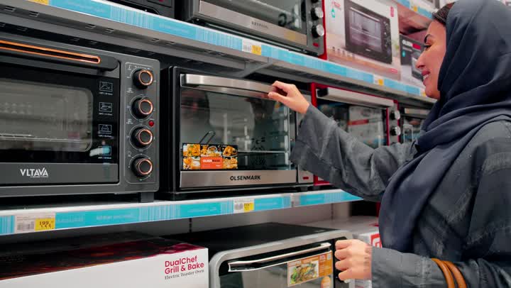 Comparing products before purchase, a close-up shot of an Emirati Gulf Arab woman wearing an abaya and hijab inspecting an electric oven, the concept of conscious buying, checking details before making a purchase decision, shopping inside an electronics store, choosing the right oven.