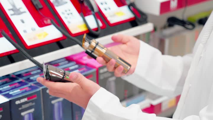 اختيار الإكسسوارات الإلكترونية المناسبة، مقارنة المنتجات التقنية الصغيرة، تصوير مقرب ليد رجل عربي خليجي يرتدي الزي التقليدي يقف داخل متجر إلكترونيات أثناء اختيار وشراء ملحقات إلكترونية، تنوع المنتجات الرقمية