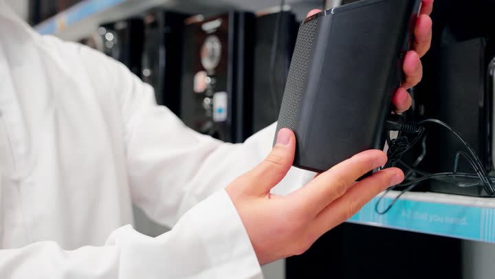 اقتناء أجهزة إلكترونية منزلية، تصوير مقرب ليد رجل عربي خليجي يرتدي الزي التقليدي يمسك مكبر صوت إلكتروني ، اختيار وشراء جهاز صوتي مناسب، مفهوم التسوق داخل المتاجر، مقارنة الأجهزة الصوتية، اختيار ملحقات إلكترونية حديثة، جودة الصوت والتقنيات الحديثة