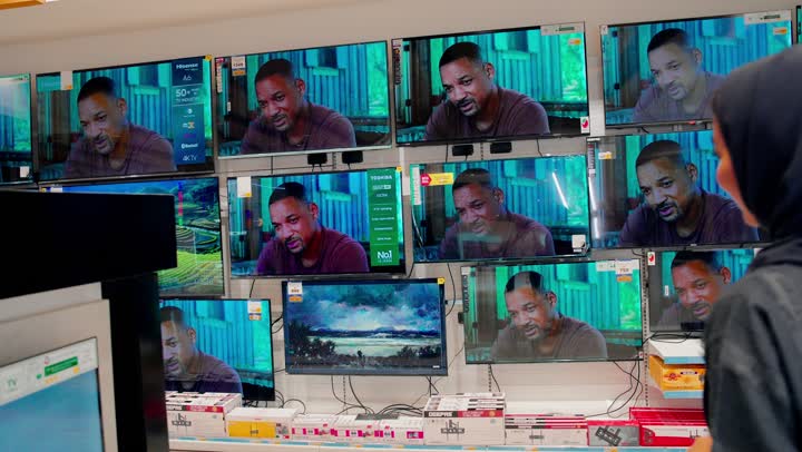 زوجان عربيان خليجيان يرتديان الزي التقليدي يقفان داخل متجر إلكترونيات ، اختيار وشراء تلفاز ذكي من بين عدة شاشات معروضة، مفهوم التسوق العائلي، مقارنة جودة الصورة وأحجام الشاشات، اقتناء الأجهزة المنزلية الحديثة، تطور تقنيات العرض الرقمية