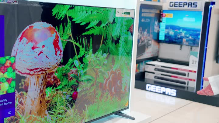 اقتناء الأجهزة المنزلية الحديثة، مفهوم التسوق داخل المتاجر، امرأة عربية خليجية ترتدي العباءة والحجاب تقف داخل متجر إلكترونيات حديث أثناء اختيار وشراء شاشة تلفاز ذكية، مقارنة أحجام الشاشات وجودة العرض، تطور التكنولوجيا الرقمية