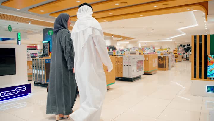 التعرف على أحدث الأجهزة التقنية، زوجان عربيان خليجيان يرتديان الزي التقليدي يتجولان داخل متجر إلكترونيات يقومان باستكشاف الأقسام المختلفة، مفهوم التسوق العائلي المشترك، الاهتمام بالتكنولوجيا الرقمية