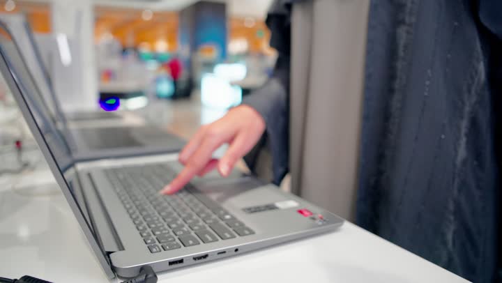 مفهوم التسوق التقني، مقارنة المواصفات التقنية، تصوير مقرب ليد امراة عربيه خليجيه اماراتية تقوم بتجربة أجهزة لابتوب معروضة داخل متجر إلكترونيات حديث، اختيار أجهزة الحاسوب المحمولة، استخدام التكنولوجيا الحديثة