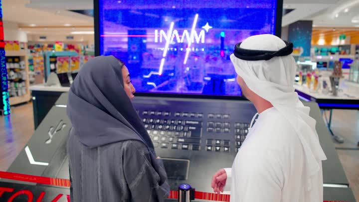 مفهوم التسوق الجماعي، رجل عربي خليجي اماراتي يرتدي الكنتدورة و الغتره يقف داخل متجر إلكترونيات حديث برفقة زوجته يتناقشان حول جهاز إلكتروني معروض، اختيار الأجهزة التقنية الحديثة، تطور التكنولوجيا الرقمية