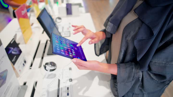 The tech shopping experience, a close-up shot of an Emirati Gulf Arab woman wearing an abaya trying out a modern tablet inside an electronics store, using smart devices, selecting suitable tech products, the evolution of digital technology.