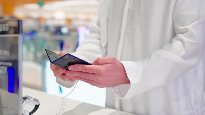 Technical shopping in Arab communities, choosing smart devices, a close-up shot of a Gulf Arab man wearing traditional attire trying out a smartphone inside a modern electronics store, the evolution of modern technology.