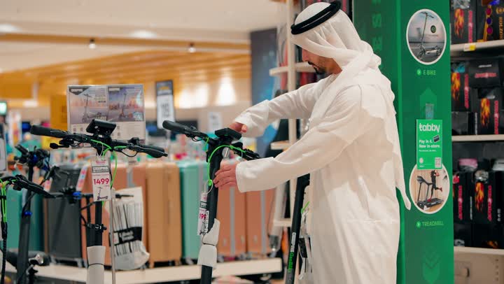 Careful selection of sports equipment, youth recreational activities, an Arab Gulf Emirati man wearing a kandura and ghutrah inspecting bicycles displayed inside the store, practicing modern sports hobbies, and focusing on a healthy lifestyle.