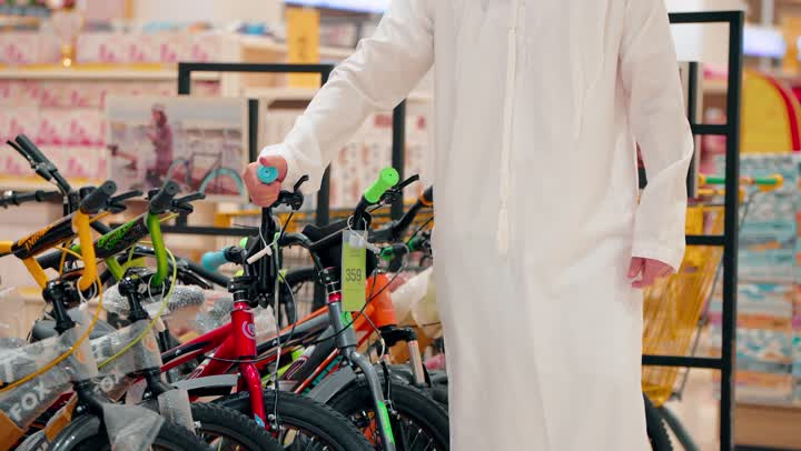 اختيار المعدات الرياضية المناسبة، الاهتمام بنمط الحياة الصحي، ممارسة الهوايات الرياضية الحديثة، تصوير مقرب ليد رجل عربي خليجي اماراتي يقوم بتفقد دراجات هوائية معروضة داخل المتجر، أنشطة ترفيهية شبابية