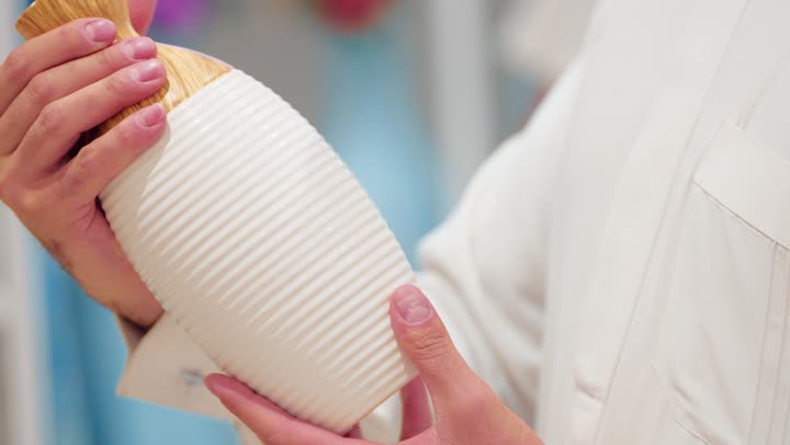 The concept of choosing modern decor, a close-up shot of the hand of an Emirati Gulf Arab woman holding an elegantly designed home decor vase inside a home supplies store, carefully examining the material and shape while shopping, paying attention to product quality and preparing the home with sophisticated aesthetic touches.