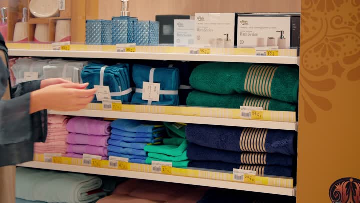 اختيار مستلزمات منزلية بعناية، تصوير مقرب لامرأة عربية خليجية اماراتية ترتدي العباءة تقوم باختيار مناشف قطنية داخل المحل، التأكد من الجودة والنعومة