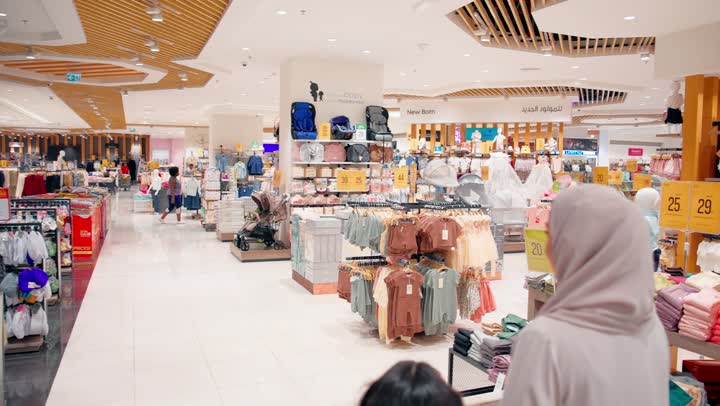 الاهتمام باختيار مستلزمات الأطفال المناسبة، تصوير من الخلف لامرأة عربية خليجيه اماراتية ترتدي العباءة و الحجاب تتجول داخل متجر للأطفال برفقة ابنتها داخل المول، استكشاف أقسام منتجات الأطفال بعناية واهتمام، مفهوم التسوق العائلي داخل المراكز التجارية