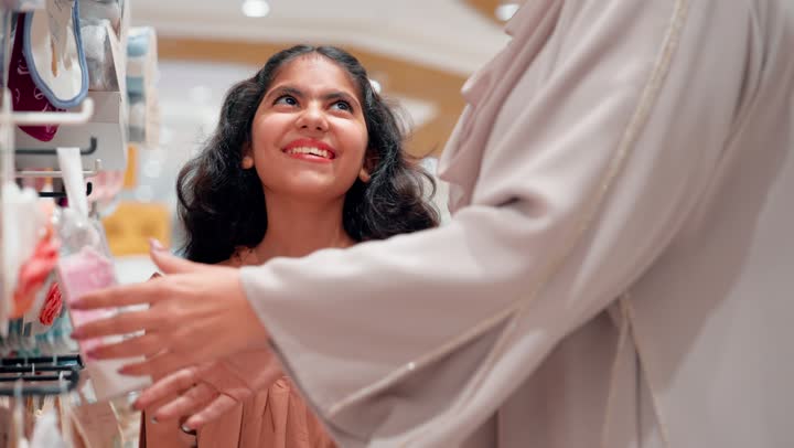 Gestures of happiness and joy, family bonding and feelings of love and care, choosing supplies for the newborn, the concept of readiness for motherhood, an Emirati Gulf Arab woman in a hijab wearing an abaya standing inside a baby supplies store with her daughter.