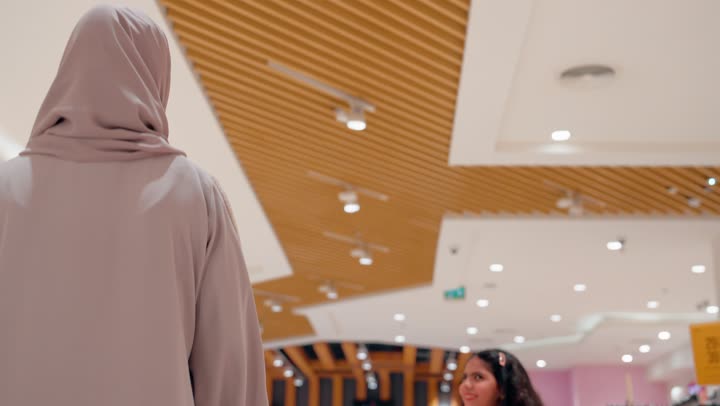 بنت عربيه خليجيه اماراتية ترتدي الزي الكاجوال تسير داخل متجر ملابس في مركز تجاري حديث برفقة والدتها، متعة التسوق داخل المولات، مفهوم التسوق العائلي، ايماءات السعادة و السرور