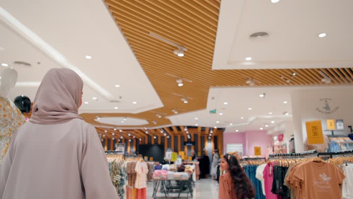 الاشارة الى شيء ما، بنت عربيه خليجيه اماراتية ترتدي الزي الكاجوال تسير داخل متجر ملابس في مركز تجاري حديث برفقة والدتها، متعة التسوق داخل المولات، مفهوم التسوق العائلي، ايماءات السعادة و السرور