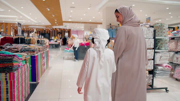العلاقة الأسرية الدافئة بين الأم والطفل، مشاعر الحب والترابط الأسري، تصوير من الخلف لأم عربية خليجيه اماراتية محجبة ترتدي العباءة تسير برفقة طفلها داخل مركز تسوق، التسوق العائلي داخل المول