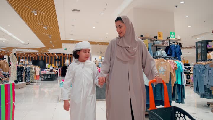 مشاعر الحب والترابط الأسري، أم عربية خليجيه اماراتية محجبة تسير برفقة طفلها داخل مركز تسوق، التسوق العائلي داخل المول، العلاقة الأسرية الدافئة بين الأم والطفل