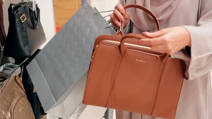 الأناقة النسائية والاهتمام بالمظهر، التسوق داخل المولات، مفهوم اختيار الإكسسوارات النسائية بعناية، تصوير مقرب لامرأة عربية خليجيه اماراتية ترتدي العباءة تقوم بتجربة حقيبة يد نسائية داخل متجر إكسسوارات