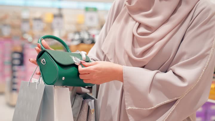 التسوق داخل المولات، مفهوم اختيار الإكسسوارات النسائية بعناية، تصوير مقرب لامرأة عربية خليجيه اماراتية ترتدي العباءة تقوم بتجربة حقيبة يد نسائية داخل متجر إكسسوارات، الأناقة النسائية والاهتمام بالمظهر