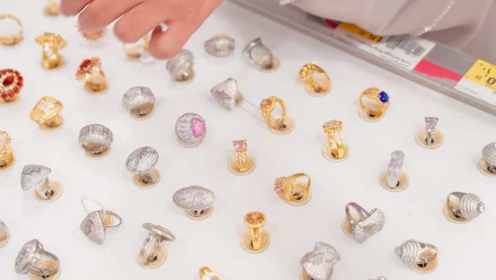 مفهوم التسوق لشراء المجوهرات النسائية، الأناقة النسائية والاهتمام بالتفاصيل، تصوير مقرب ليد امراه عربية خليجية اماراتية تقوم باختيار خاتم ذهبي من مجموعة مجوهرات معروضة داخل  المتجر، اختيار الإكسسوارات الفاخرة بعناية