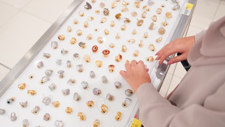 الأناقة النسائية والاهتمام بالتفاصيل، تصوير مقرب لامرأة عربية خليجية اماراتية تقوم باختيار خاتم ذهبي من مجموعة مجوهرات معروضة داخل  المتجر، مفهوم التسوق لشراء المجوهرات النسائية، اختيار الإكسسوارات الفاخرة بعناية