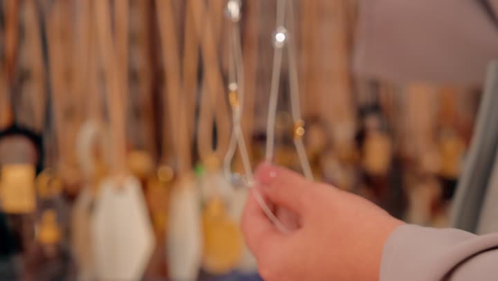 الأناقة النسائية والاهتمام بالمظهر، التسوق داخل مول تجاري حديث، تصوير مقرب ليد امراة عربية خليجية اماراتية  تقوم باختيار إكسسوارات نسائية، تفقد سلاسل وقلائد معلقة بعناية أثناء التسوق