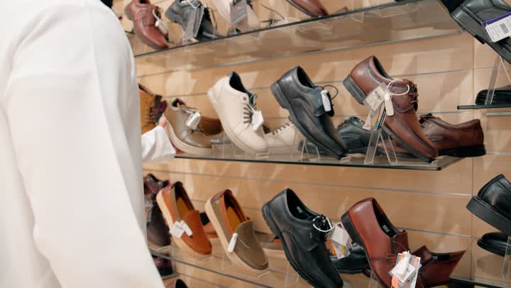The concept of men's elegance and conservative fashion, a close-up shot of an Emirati Gulf Arab man wearing a kandura shopping among a variety of men's shoes, attention to detail and product quality, selecting shoes inside a retail store.