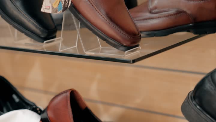 تصوير مقرب ليد رجل عربي خليجي إماراتي يرتدي الكندورة يتسوق بين تشكيلة متنوعة من الأحذية الرجالية، اهتمام بالتفاصيل وجودة المنتج، اختيار الأحذية داخل متجر تجزئة