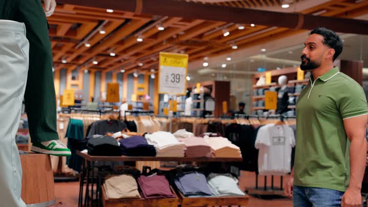 التدقيق في اختيار المنتجات قبل إتمام الشراء، شاب عربي خليجي اماراتي يرتدي الزي الكاجوال يقوم بتفقد جودة الأقمشة ومقاسات الملابس الجاهزة، التسوق داخل متجر ملابس رجالي