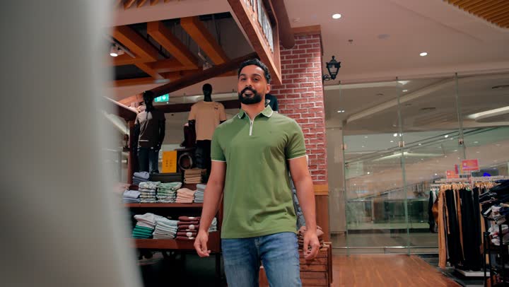 التسوق داخل متجر ملابس رجالي، مفهوم التسوق الواعي والانتباه للتفاصيل، اختيار دقيق للمنتجات قبل الشراء، شاب عربي خليجي اماراتي يرتدي الزي الكاجوال يقوم بتفقد جودة الأقمشة ومقاسات الملابس الجاهزة