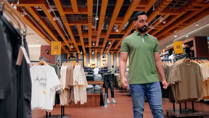 التسوق داخل متجر ملابس رجالي، التركيز على جودة الأقمشة وتنوع الخيارات، مفهوم التسوق والاختيار بعناية، شاب عربي خليجي اماراتي  يرتدي الزي الكاجوال يتفحص بنطال مطوي على الرفوف