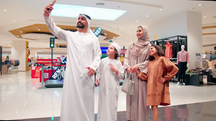 التقاط صورة تذكارية عبر الهاتف المحمول، عائلة عربية خليجية إماراتية توثق لحظاتها السعيدة أثناء التجول في المول، مفهوم الترابط الأسري والحياة العصرية، ايماءات السعادة والسرور