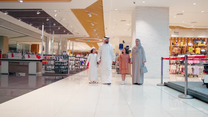 The concept of family and shopping in modern malls, spending enjoyable family time while shopping, an Arab Gulf Emirati father and mother dressed in traditional attire walking with their children inside a modern shopping center.