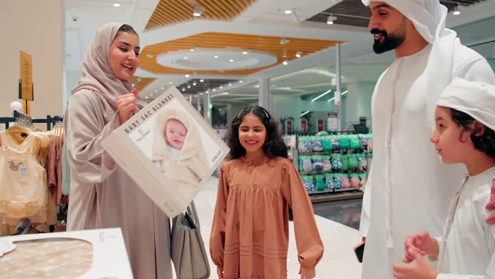 مفهوم التسوق العائلي والاستعداد للطفل، اختيار منتجات العناية بالمواليد، عائلة عربية خليجية اماراتية ترتدي الزي التقليدي داخل مركز تسوق تتفقد بطانية أطفال حديثي الولادة