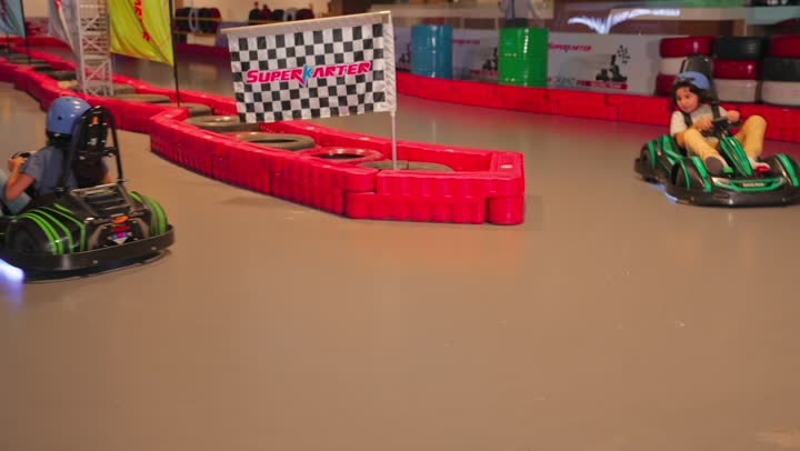 Two Arab Gulf Emirati children are enjoying driving go-karts inside a modern amusement park, a recreational car race for children, a concept of entertainment and safe competition.