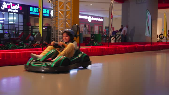 Entertainment and competition in a safe environment, a recreational car race for children, two Arab Gulf Emirati children enjoying driving go-karts inside a modern amusement park.