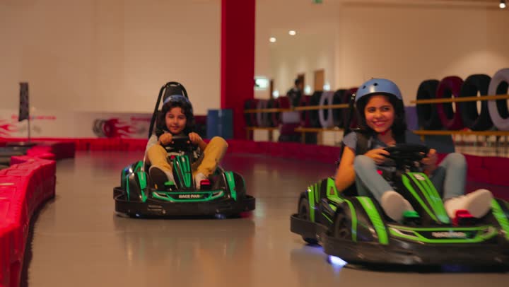 التسلية بروح التنافس الآمن، سباق سيارات ترفيهي للأطفال، طفلان عربيان خليجيان اماراتيان يستمتعان بقيادة سيارات الكارتينج داخل مدينة ألعاب حديثة