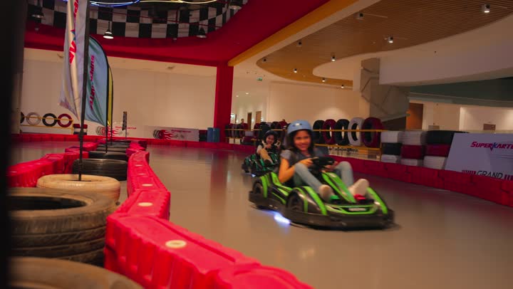 مفهوم المرح والتنافس الآمن، سباق سيارات ترفيهي للأطفال، طفلان عربيان خليجيان اماراتيان يستمتعان بقيادة سيارات الكارتينج داخل مدينة ألعاب حديثة