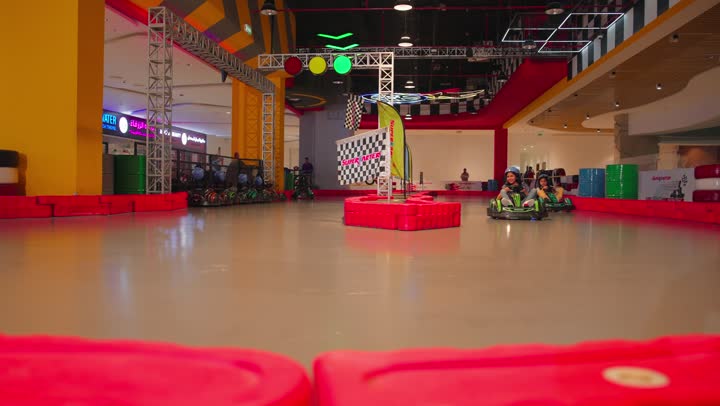 Recreational activities based on safe competition, a fun car race for children, two Emirati Gulf Arab children enjoying driving go-karts inside a modern amusement park.