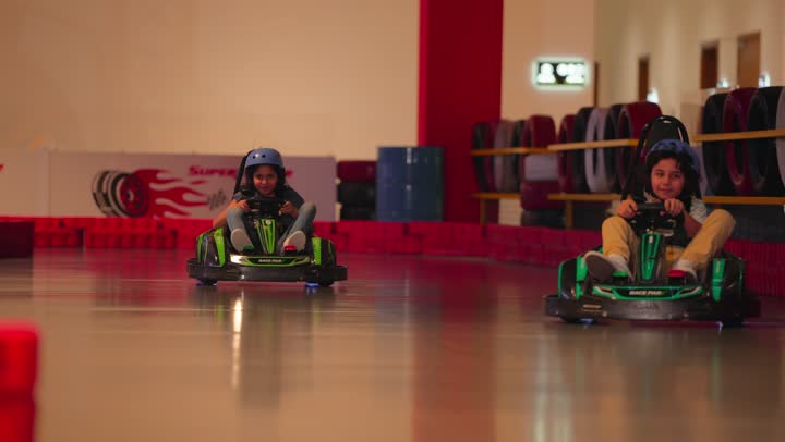 Combining entertainment with a spirit of safe competition, a recreational car race for children, two Arab Gulf Emirati children enjoying driving go-karts inside a modern amusement park.