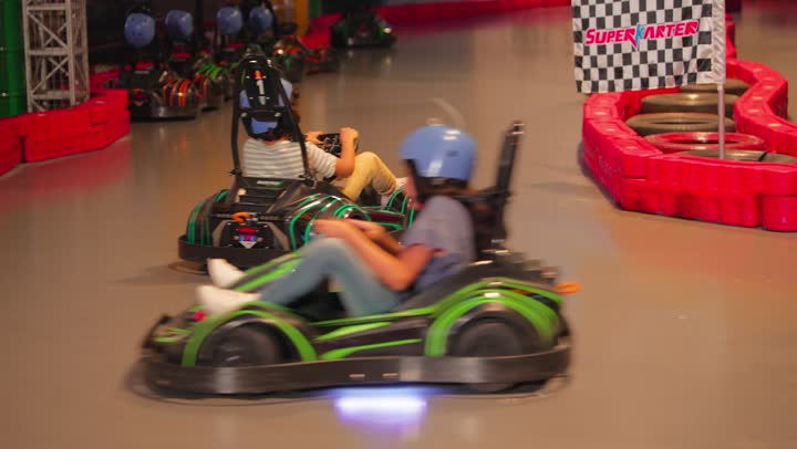 سباق سيارات ترفيهي للأطفال، طفلان عربيان خليجيان اماراتيان يستمتعان بقيادة سيارات الكارتينج داخل مدينة ألعاب حديثة، مفهوم الترفيه والتنافس الآمن