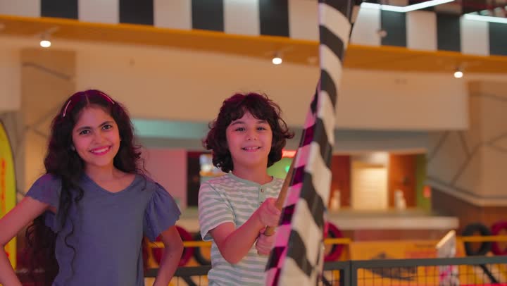 مفهوم التحدي والفوز، ولد عربي خليجي اماراتي يرتدي الزي الكاجوال يحمل علم النهاية لسباق السيارات داخل مدينة ألعاب برفقة اخته، الاستمتاع بالأجواء الترفيهية المليئة بالحيوية