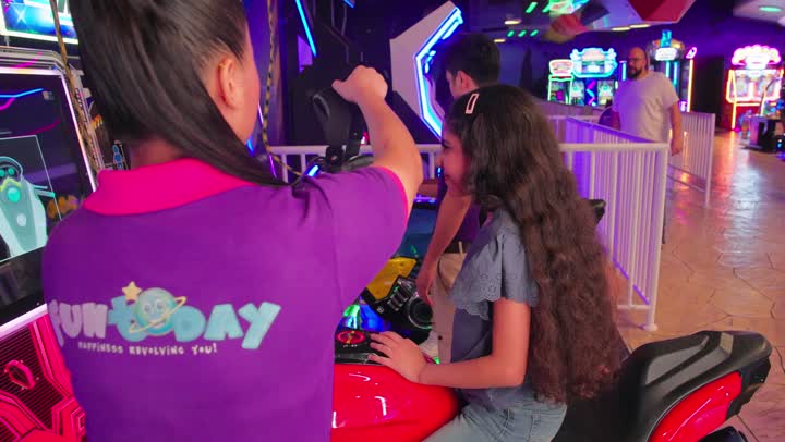 بنت عربية خليجية اماراتية ترتدي الزي الكاجوال تخوض لعبة الواقع الافتراضي بمساعدة مشرفة داخل مركز ترفيهي حديث، أجواء مليئة بالحماس والتكنولوجيا الحديثة، أنشطة ترفيهية للأطفال