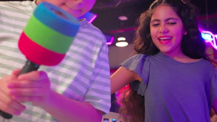 مفهوم الترفيه والتسلية للأطفال، ولدعربي خليجي اماراتي يرتدي الزي الكاجوال يستخدم المطرقة في لعبة ضرب الدمى التفاعلية برفقة اخته، ايماءات  السعادة والمرح داخل صالة ألعاب إلكترونية