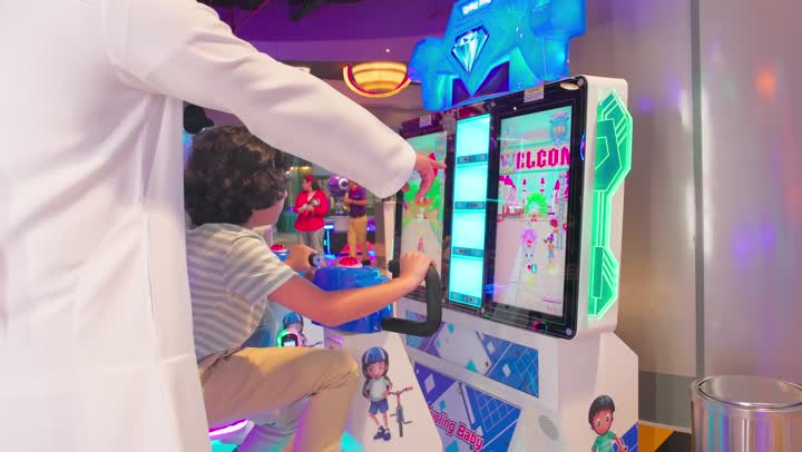 Recreational activities for children inside amusement parks, the concept of entertainment and fun, an Emirati Gulf Arab boy wearing casual attire enjoying playing the electronic game Pogo Jump inside a recreational center with his father.