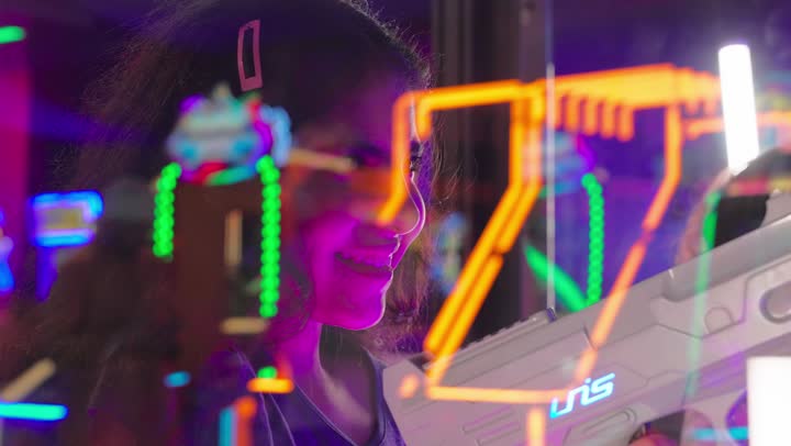 تصوير مقرب لبنت عربية خليجيه اماراتية تمسك مسدس اللعبة وتوجه التصويب نحو الشاشة بتركيز وحماس، لعبة التصويب الإلكترونية داخل صالة ألعاب ترفيهية، ايماءات السعادة و السرور