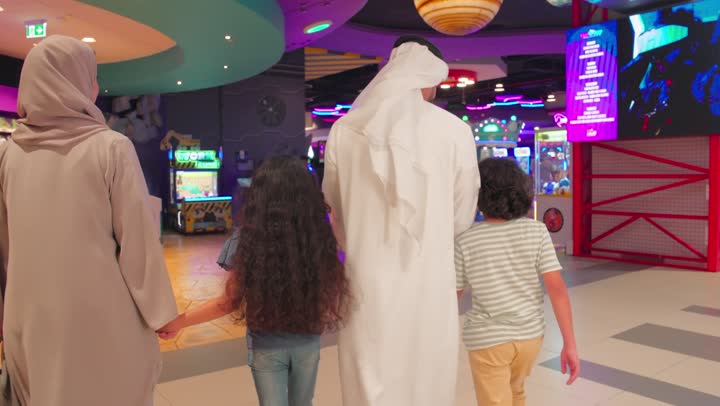 قضاء أوقات سعيده في أرض المرح، مفهوم التسلية والترفيه، تصوير من الخلف لدخول عائلة عربية خليجية اماراتية إلى مركز ألعاب إلكترونية حديث داخل مجمع تجاري، المراكز الترفيهيه المسلية في الامارات العربية