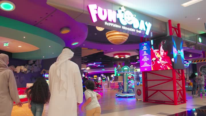 The concept of entertainment and amusement, a rear view of an Emirati Gulf Arab family entering a modern electronic games center inside a shopping mall, the entertaining recreational centers in the United Arab Emirates, spending happy times in the land of fun.