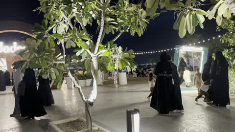 A nighttime shot of a seating area with hanging lights and small trees, famous tourist landmarks, the tourist waterfront in the Kingdom of Saudi Arabia in the city of Jubail Industrial, Jubail Corniche, a collection of restaurants and cafes overlooking the sea.